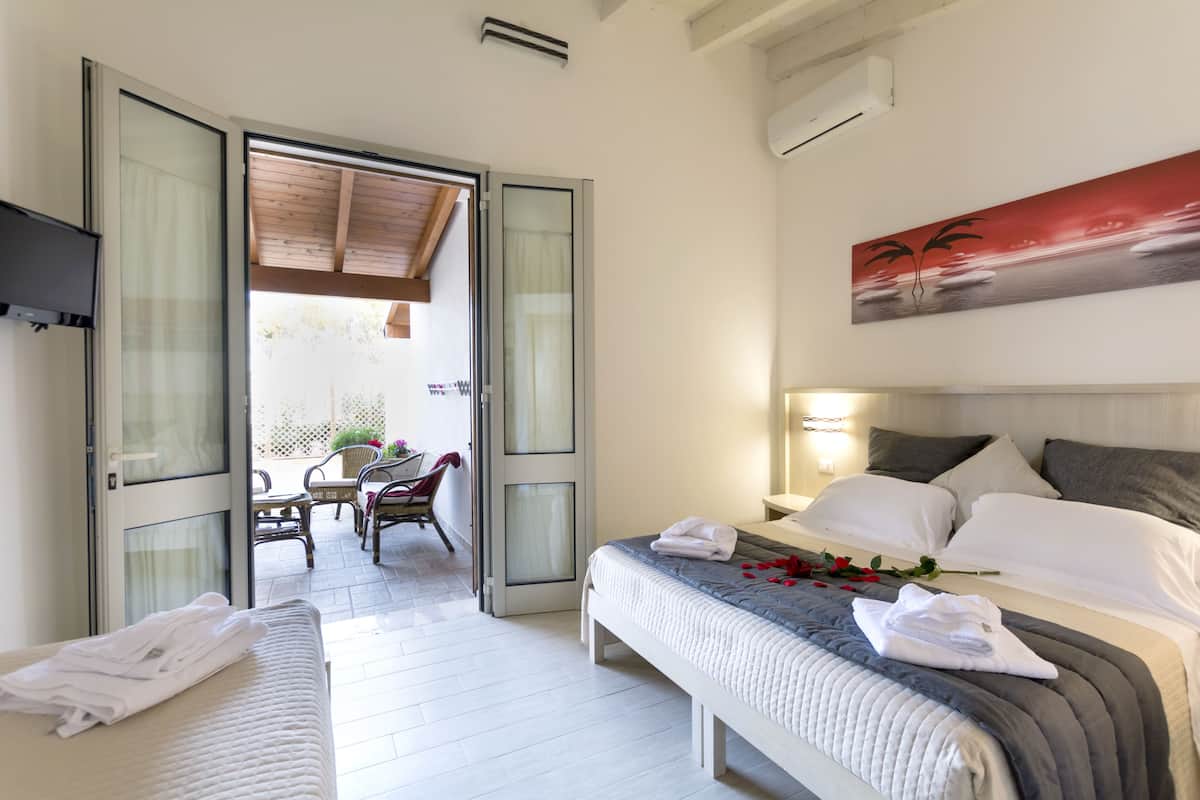 A hotel room with two beds, a painting, and a view of the outside.