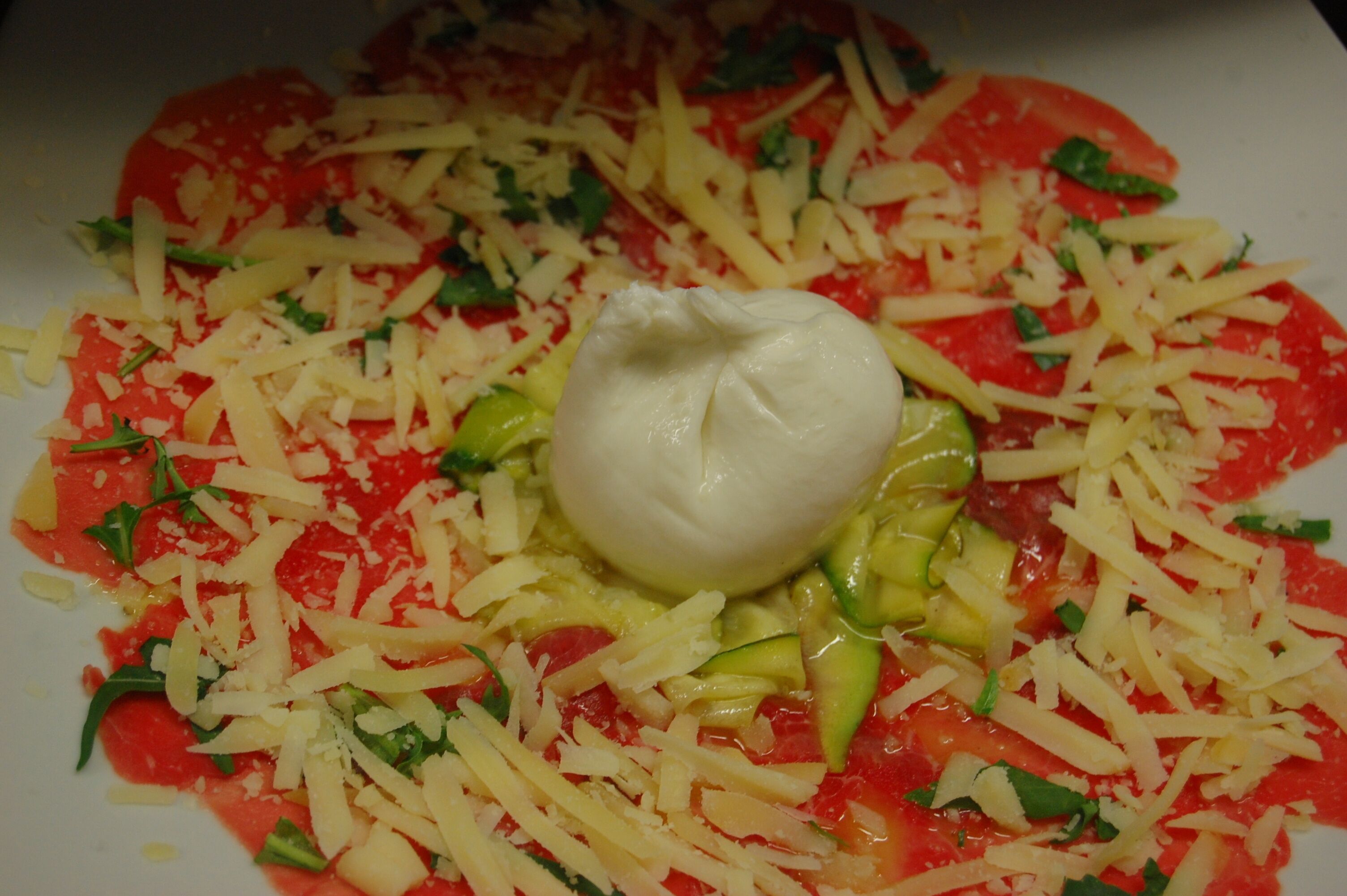 A plate of food with a tomato-based dish, cheese, and a dollop of cream.