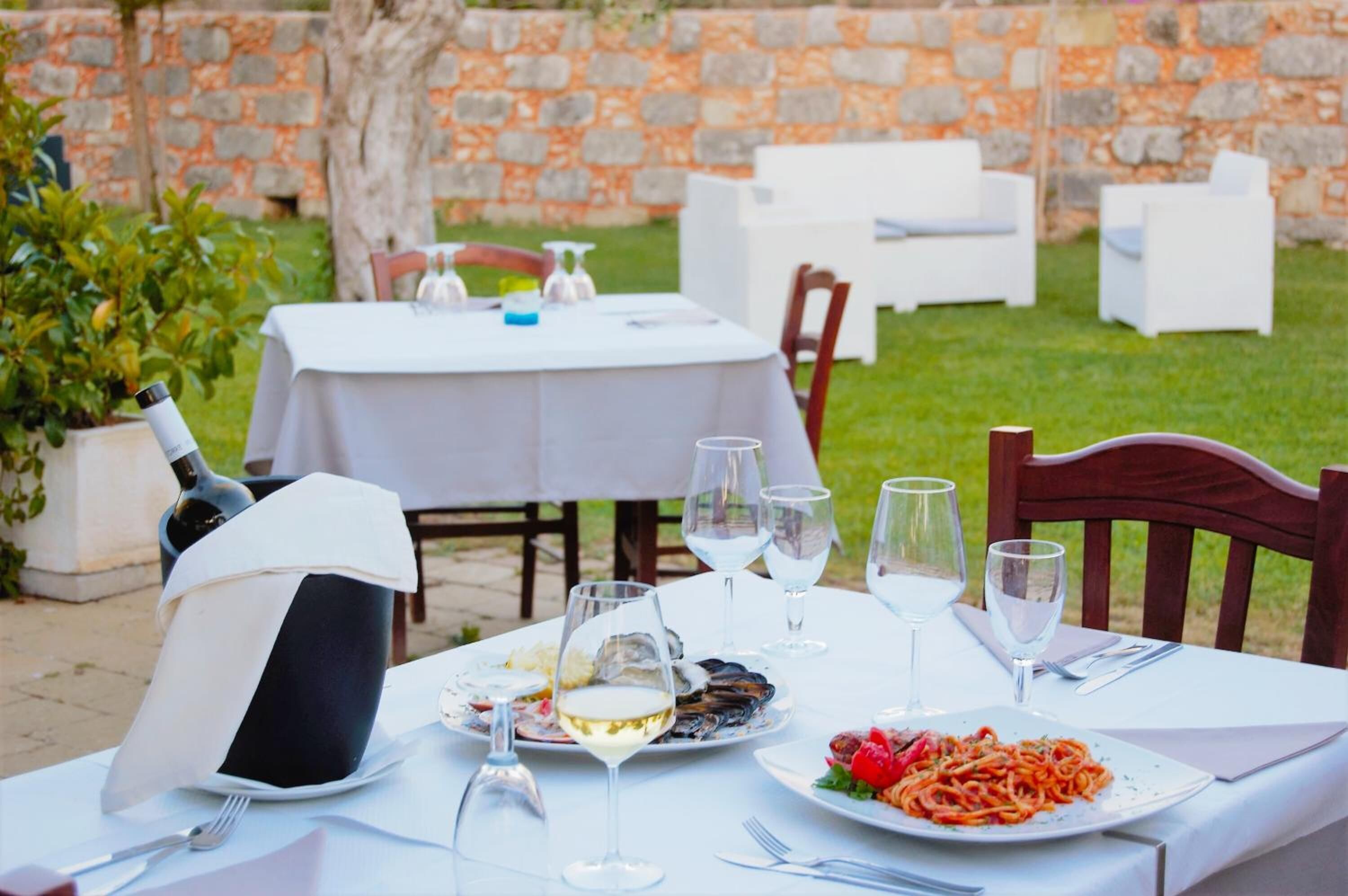 Un área de comedor al aire libre con una mesa dispuesta para una comida, que incluye platos de comida y copas de vino.