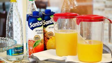 Una bandeja con diversas bebidas, incluyendo una botella de agua S. Bernardo, dos cartones de jugo de piña Santol Santo y una jarra de jugo de naranja.