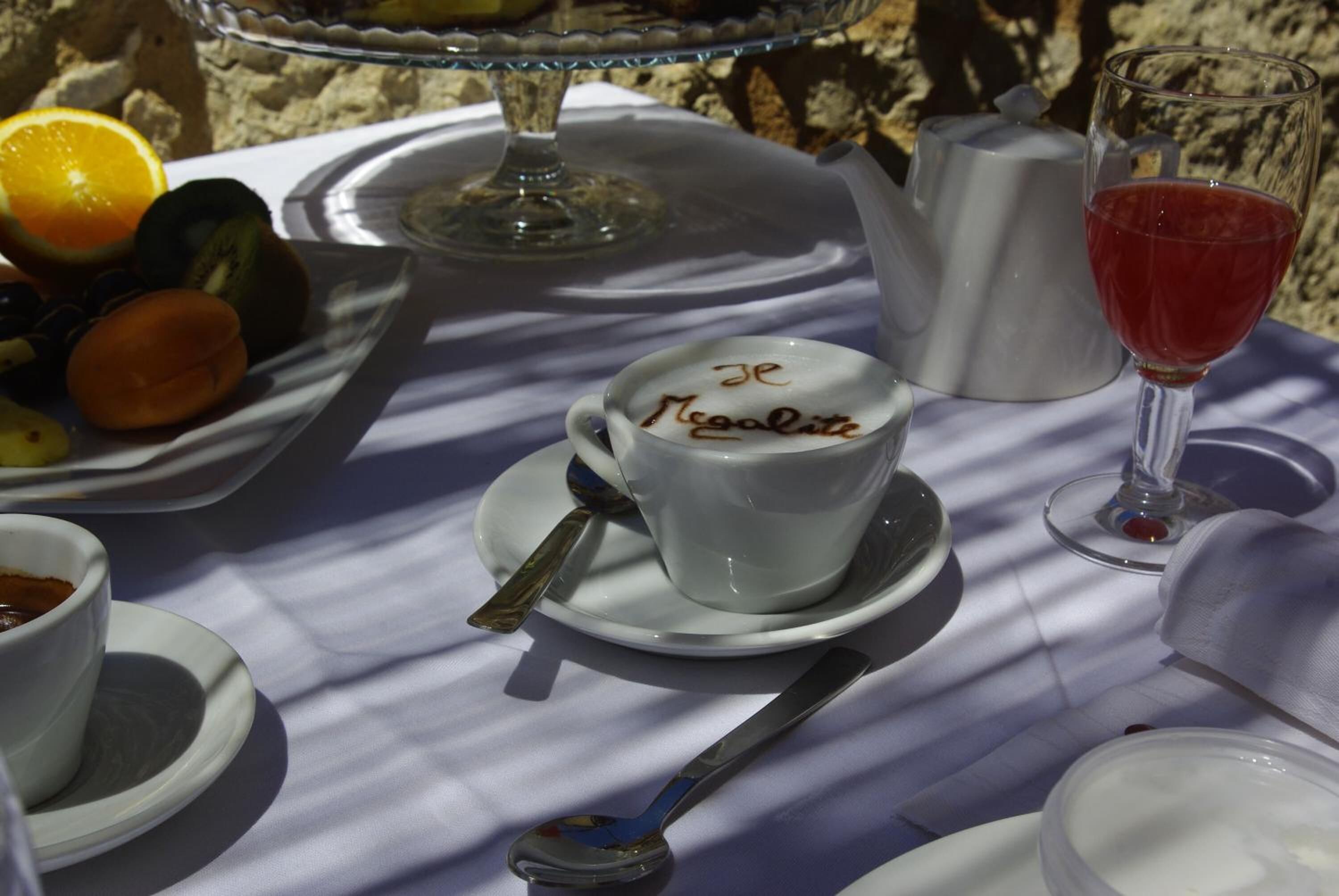 Ein Tisch mit einer weißen Tasse mit der Aufschrift 'Je Ne Regrette', einem Glas Rotwein und einer Fruchtschale.