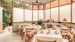 Une véranda aménagée avec des tables et des chaises, un buffet proposant une variété de plats et de boissons, et des plantes en pot.