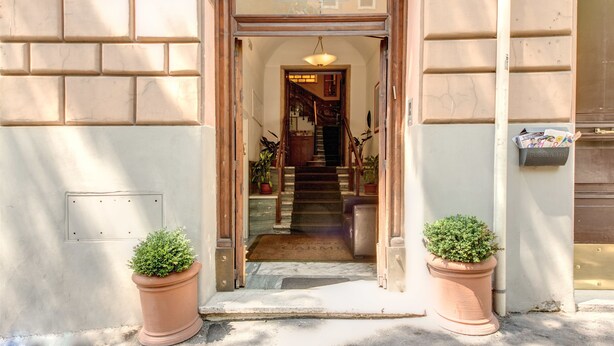 Une entrée d’immeuble avec une porte en bois, un escalier menant à l’intérieur et deux plantes en pot de chaque côté.
