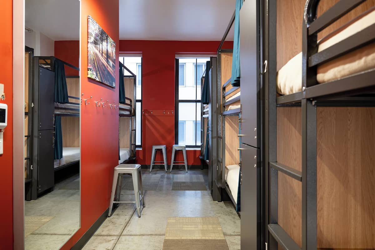 A dormitory room with bunk beds, a small stool, and a window.