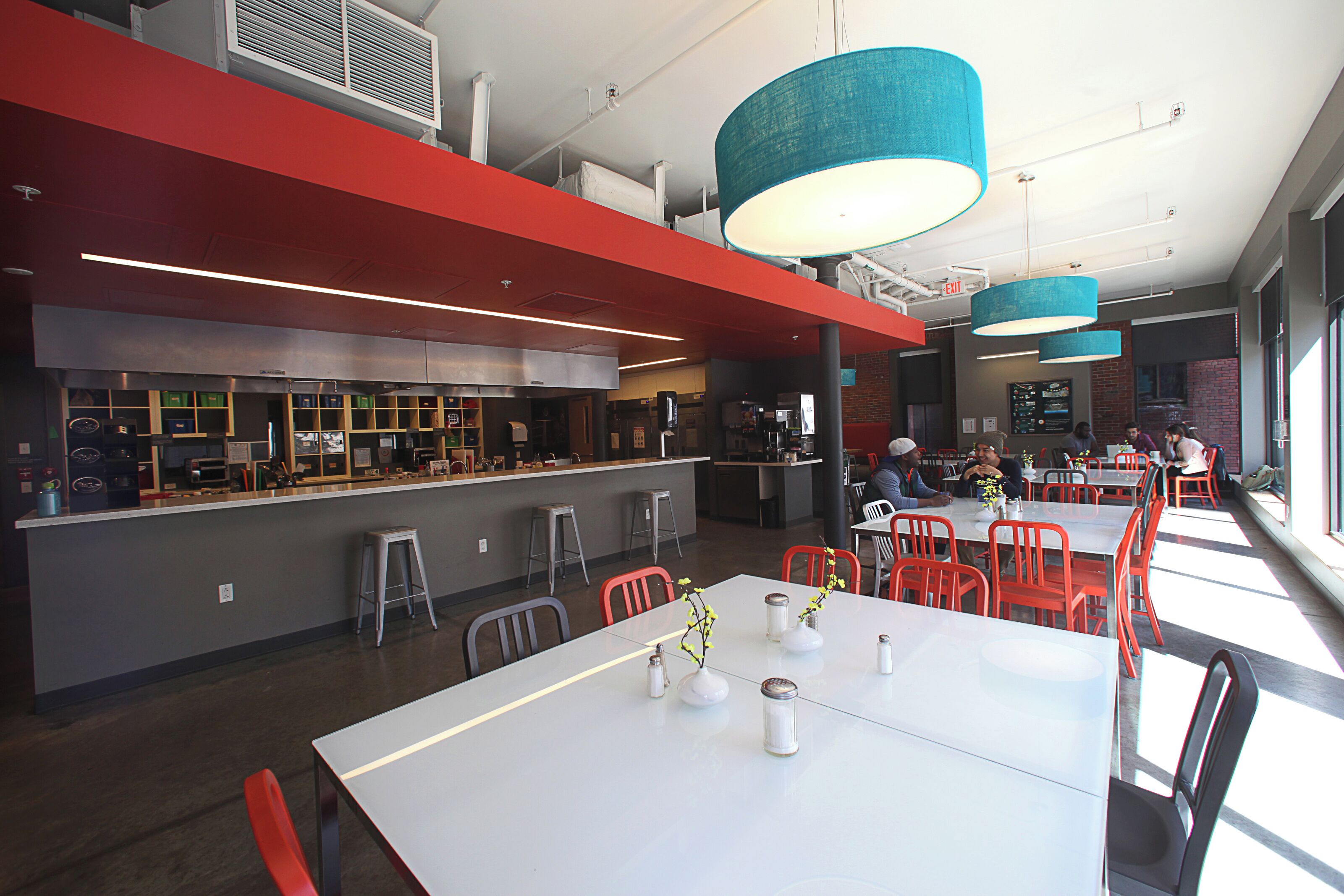 A modern restaurant with white tables, red chairs, and blue hanging lamps.