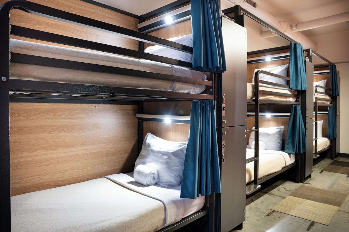 A row of bunk beds with wooden headboards and blue curtains, arranged in a narrow corridor.