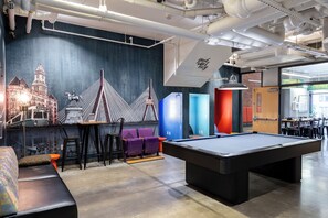 A pool table in a room with a mural of a cityscape, purple chairs, and a sofa.