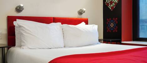 A hotel room with a red headboard, white bedding, and a decorative wall panel.