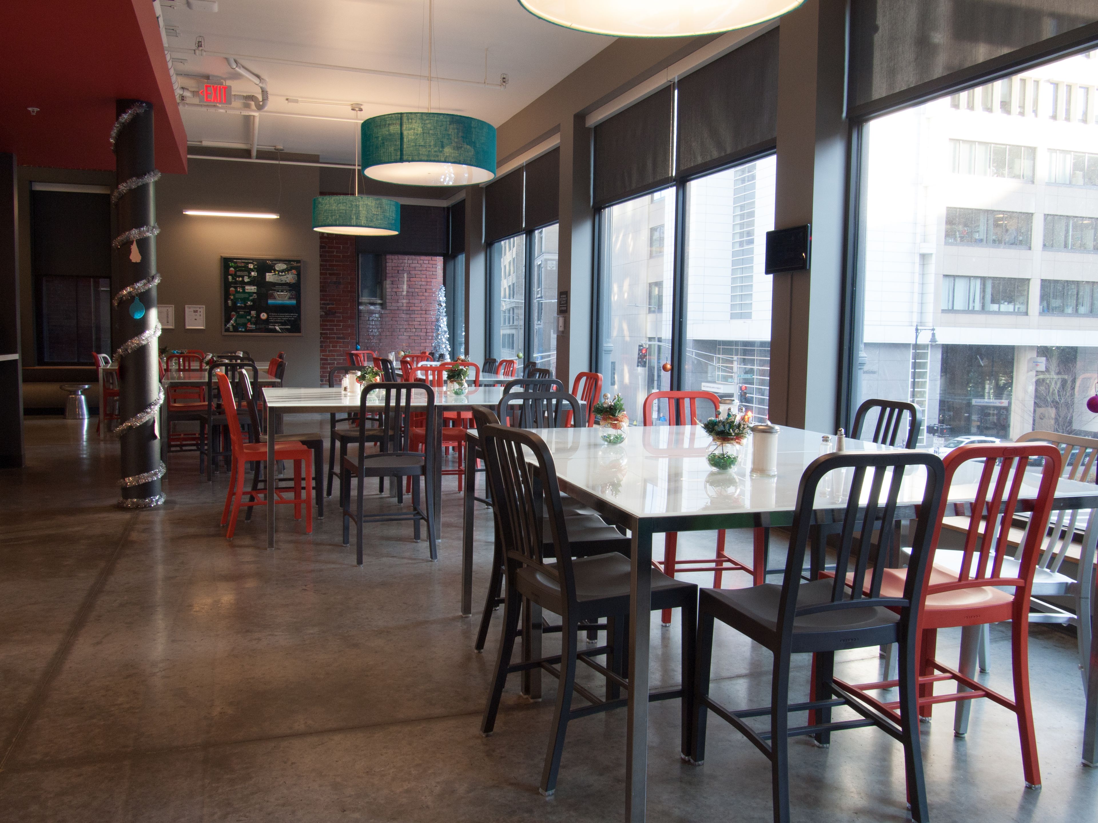Un comedor moderno con una mesa larga, sillas rojas y negras, y ventanas grandes que ofrecen vistas a la ciudad.