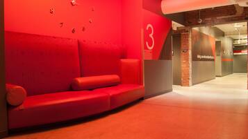 Une salle d’attente aux murs rouges, avec un canapé, une horloge et un panneau indiquant le numéro « 3 ».