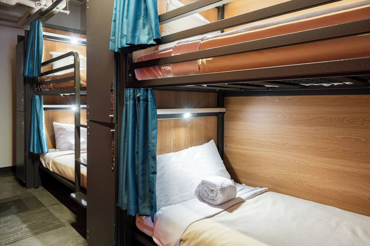 A bunk bed room with a wooden headboard, a rolled towel on the lower bunk, and blue curtains on the upper bunk.