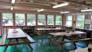 A dining area with picnic tables and benches, large windows, and a green floor. - HI Eastham - Hostel (Eastham)
