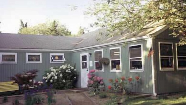 A single-story house with a front porch, a small garden with various plants and flowers, and a bench. - HI Eastham - Hostel (Eastham)