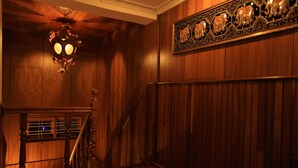 A wooden interior with a staircase, a chandelier, and a decorative wall piece. - The Hotel Emperor (Mandalay)