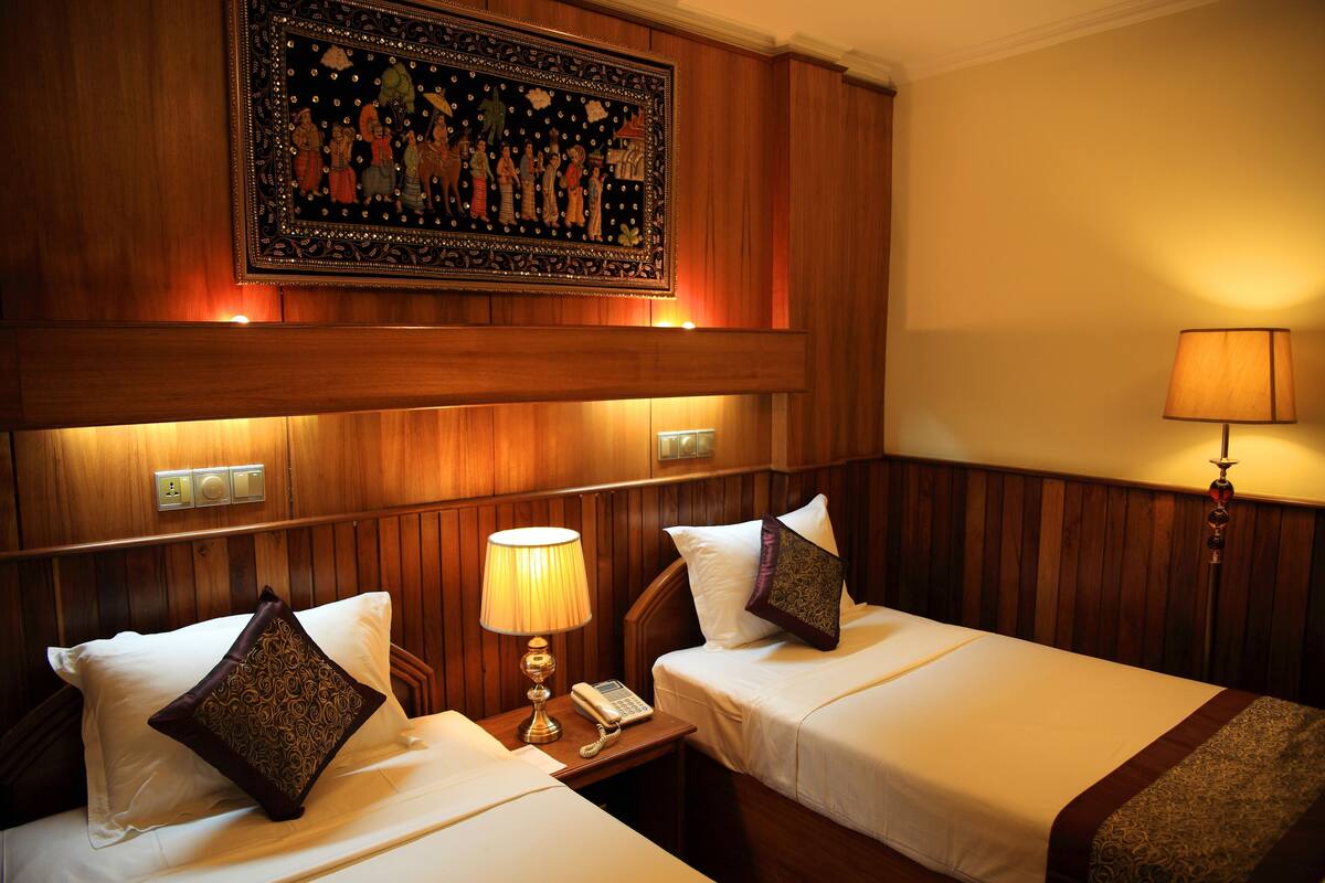 A hotel room with two beds, a nightstand with a lamp, a telephone, and a decorative wall hanging.