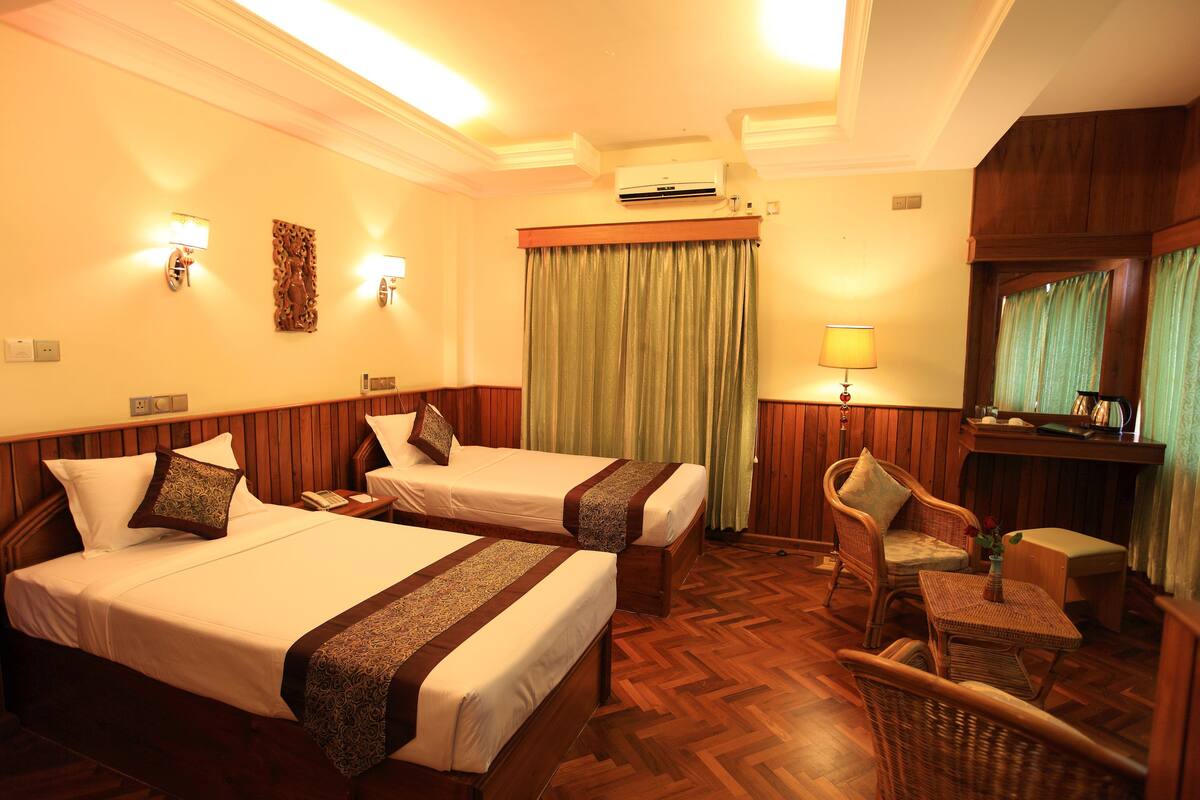 A hotel room with two beds, a chair, a small table, and a desk with a lamp.