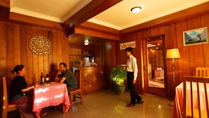 A wooden interior with a dining table, chairs, a potted plant, and a reception area. - The Hotel Emperor (Mandalay)