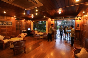 A wooden-floored room with wicker furniture, a small round table, and a television. - The Hotel Emperor (Mandalay)