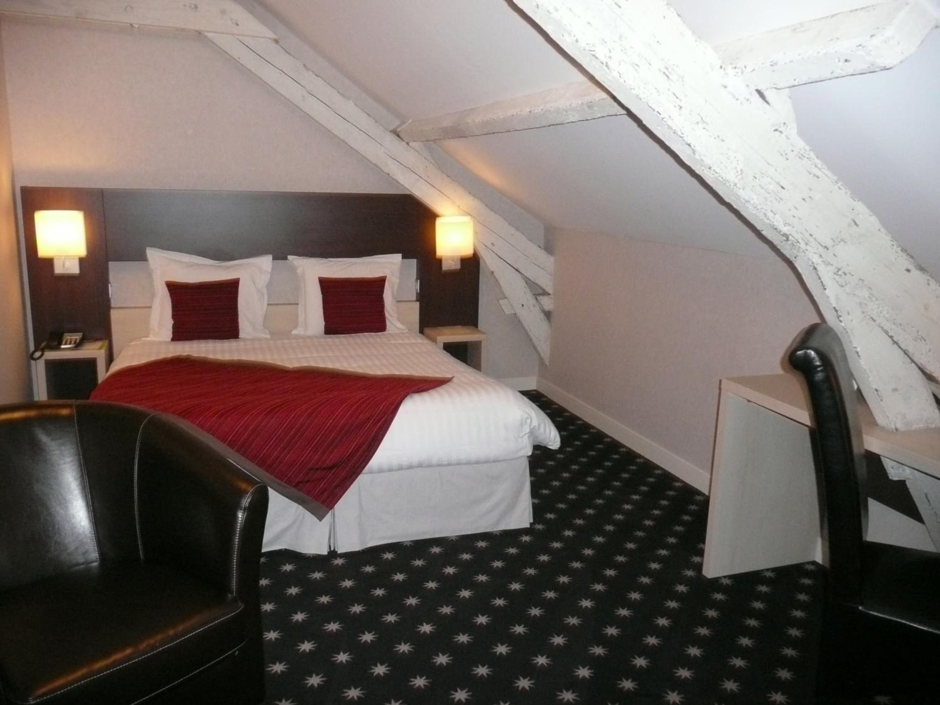 Quarto de hotel com uma cama, duas mesas de cabeceira, uma cadeira e uma escrivaninha.