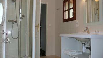 Une salle de bain avec une douche à parois de verre, un lavabo blanc avec un miroir et un porte-serviettes.