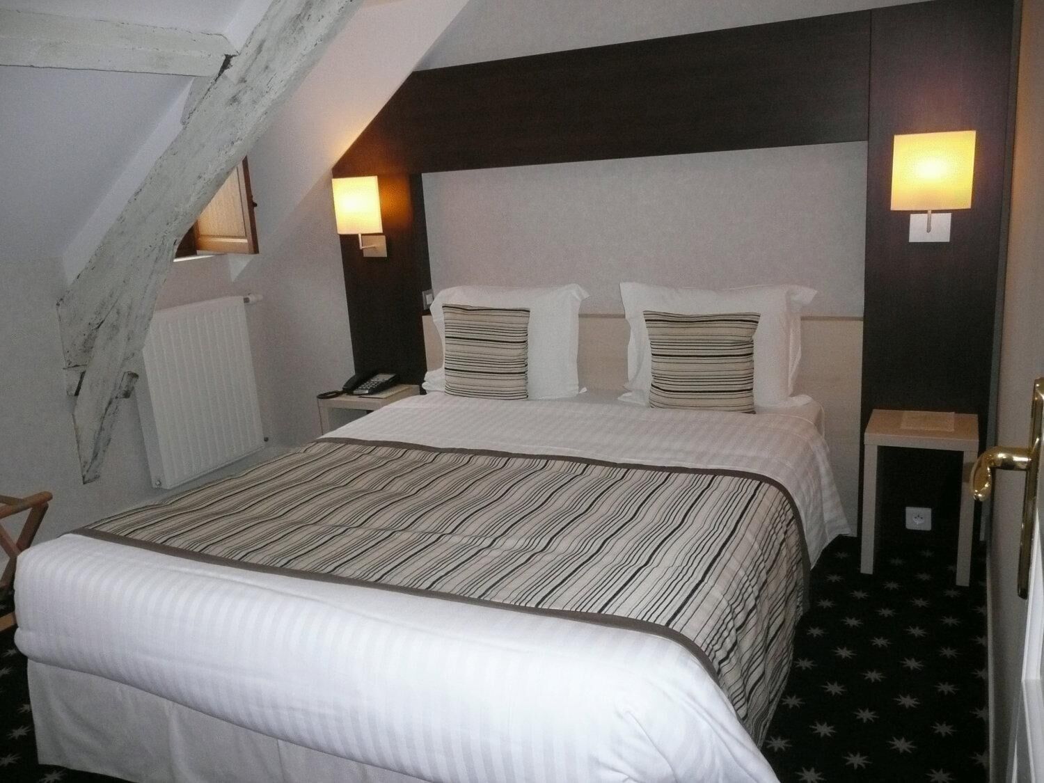 Ett hotellrum med en säng, ett nattduksbord, en lampa och ett element.