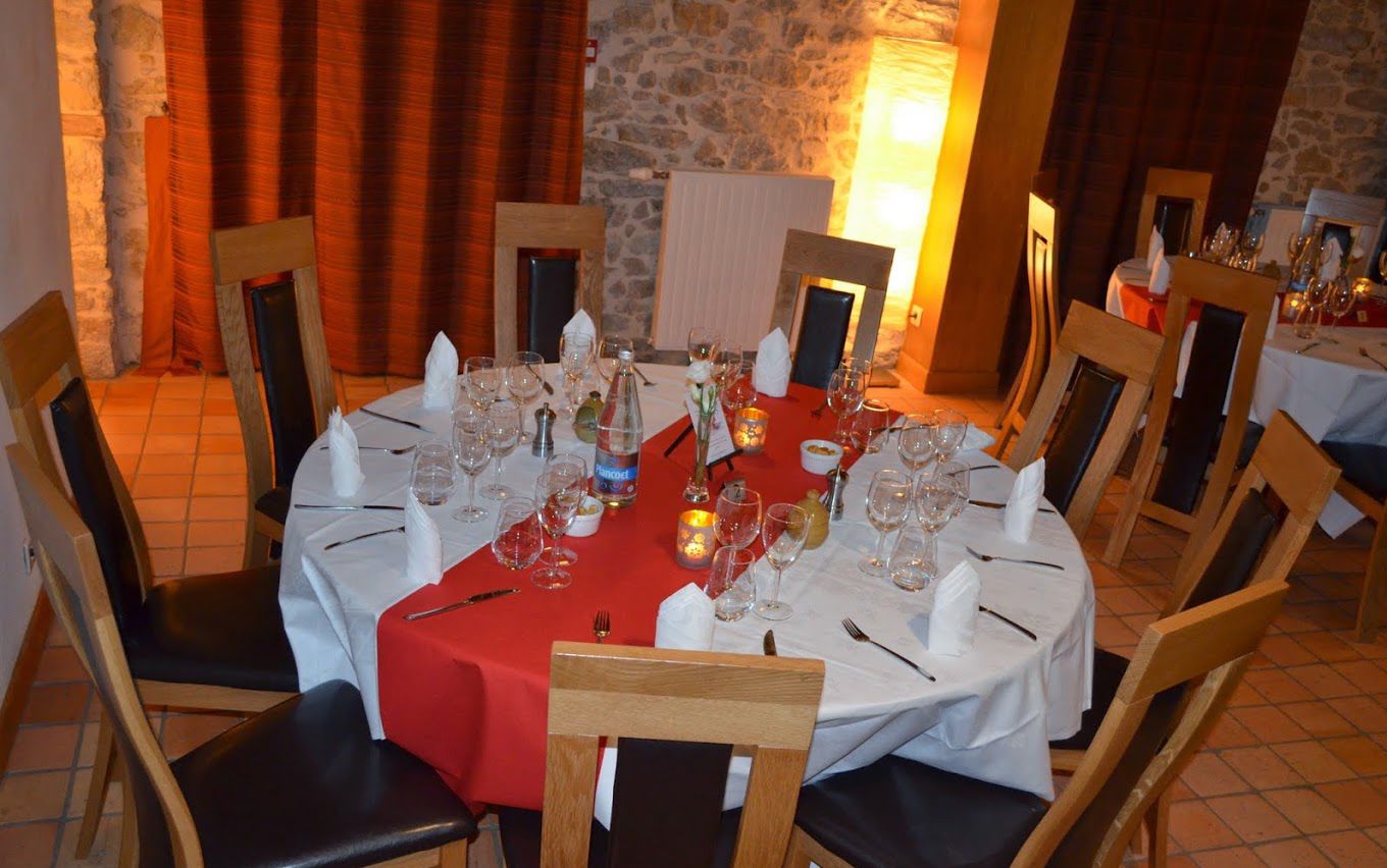 A round dining table set for a meal with white tablecloths, wooden chairs, and a stone wall in the background.