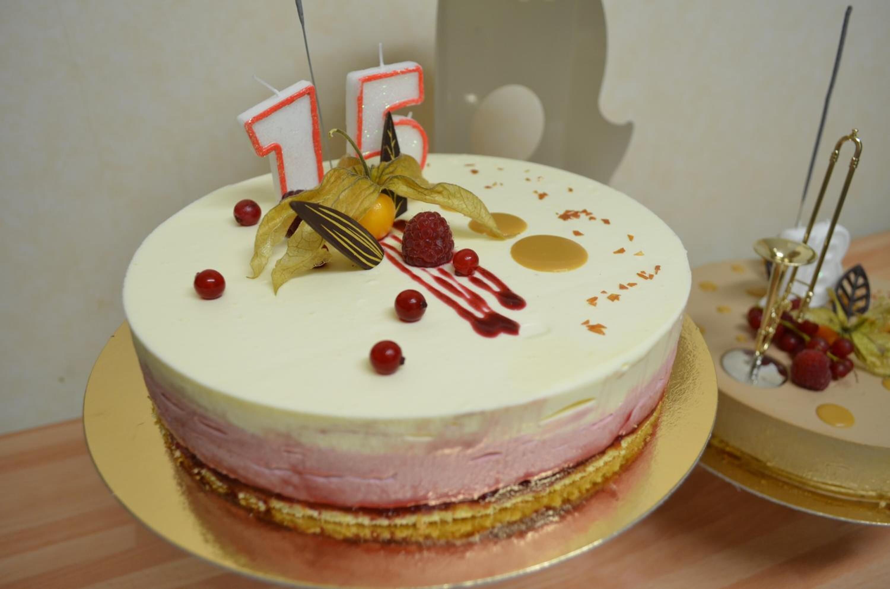 A round cake with white frosting, decorated with red berries, a dried flower, and a candle shaped like the number 15.
