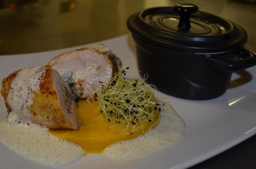 A plate with a piece of meat, a yellow sauce, and a small pot.