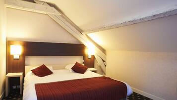 Habitación de hotel con cama, dos lámparas de noche, cabecero de madera y techo inclinado.