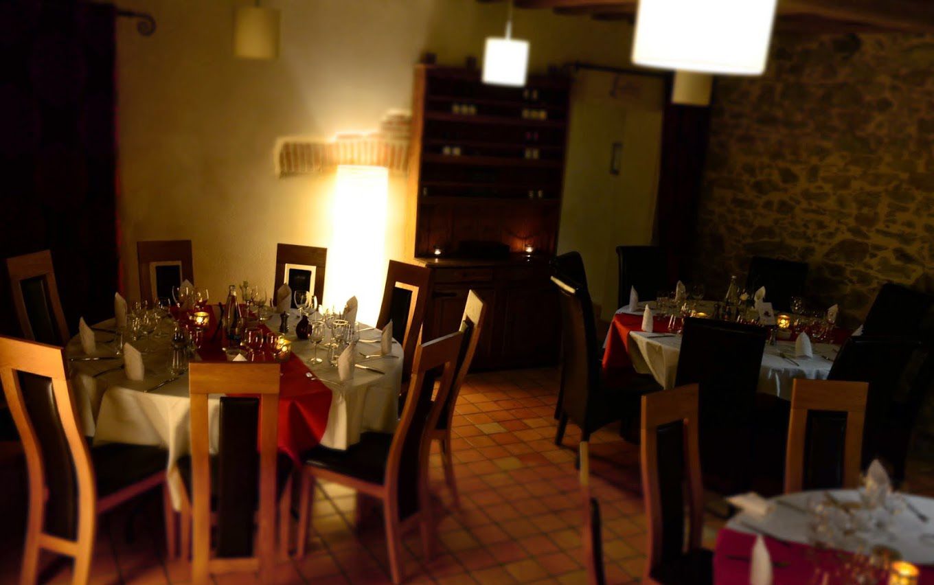A dimly lit restaurant with tables set for dining, featuring a stone wall and wooden furniture.
