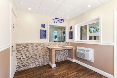 A hotel reception area with a tiled wall, a reception desk, a window with a view, and a wall-mounted air conditioning unit.