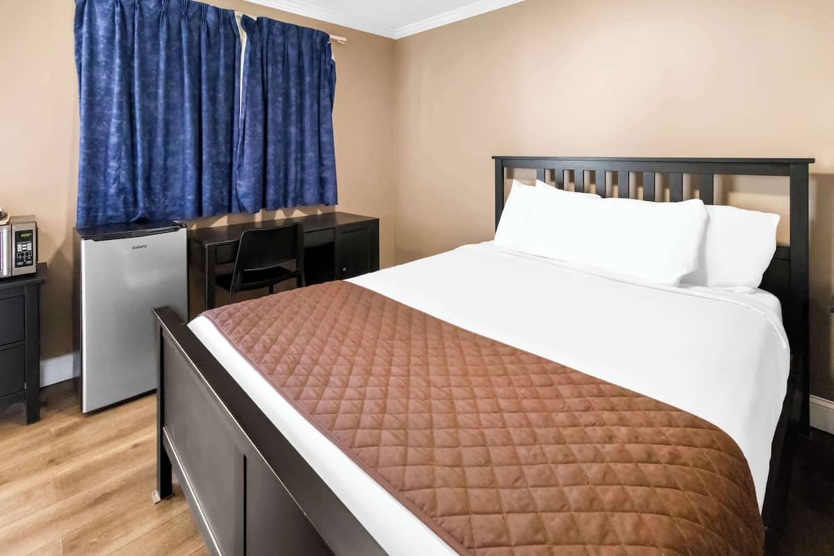 A hotel room with a bed, a desk with a computer, a refrigerator, and a window with curtains.