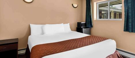 A hotel room with a large bed, a bedside table, a TV, and a window with curtains.