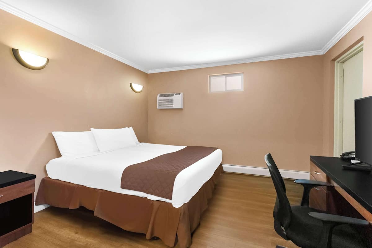 A hotel room with a bed, a desk, a chair, and a television.