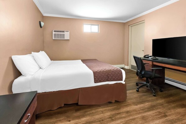 A hotel room with a bed, a desk, a chair, a television, and an air conditioning unit.