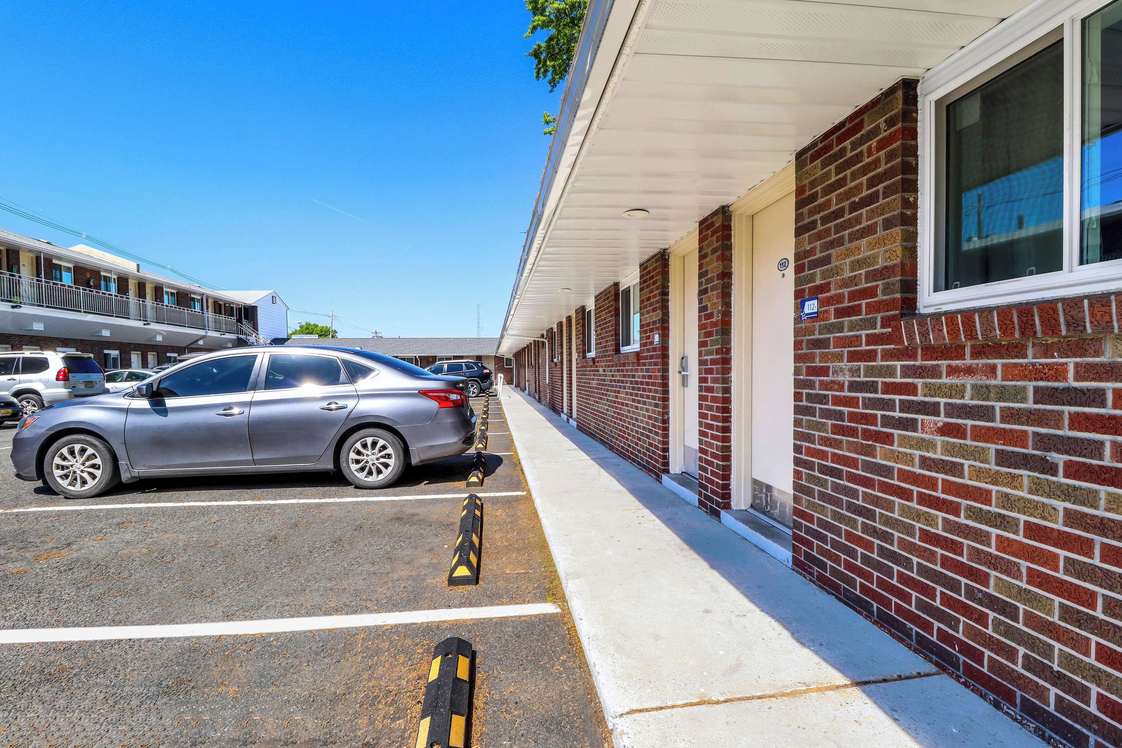 A parking lot with a silver car parked in front of a building with a brick facade and a white awning.