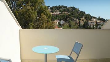 Een balkon met een tafel en twee stoelen, met uitzicht op een heuvel waarop gebouwen staan.