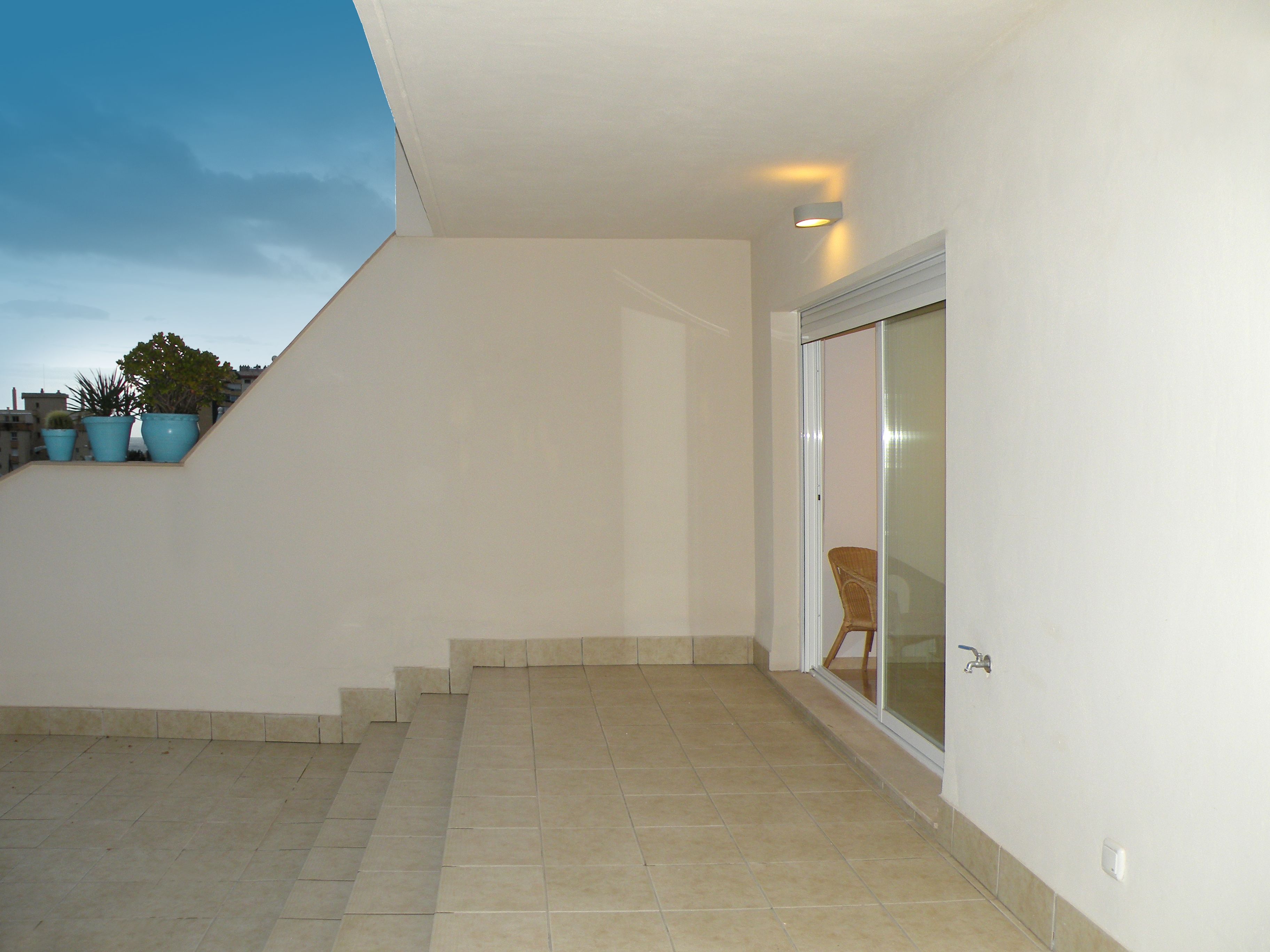 Un espacio exterior limpio y moderno con suelo de baldosas y una escalera que conduce a un acceso de vidrio.