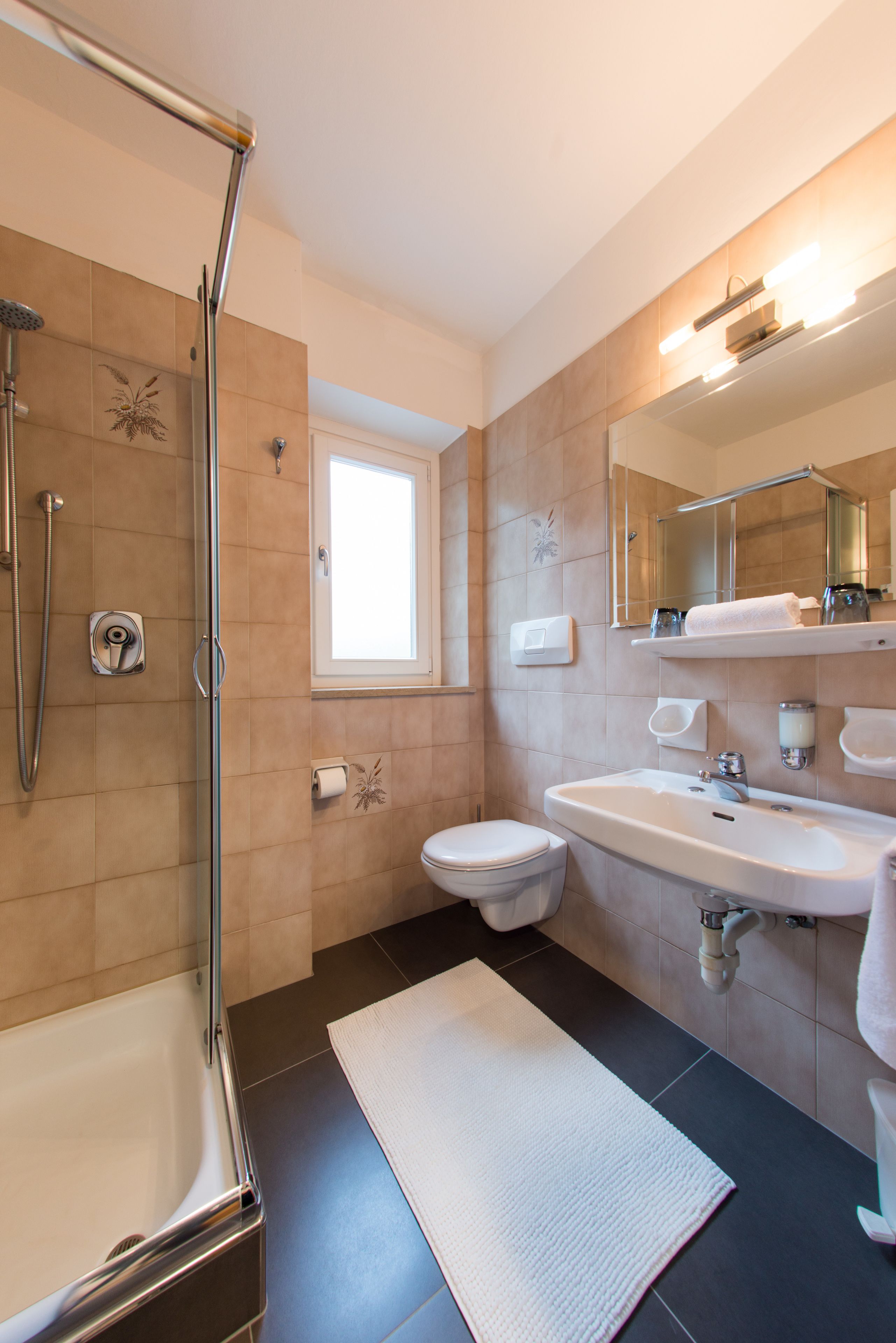 Un baño moderno con ducha de vidrio, inodoro blanco, lavamanos y un espejo grande.