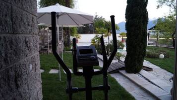 Eine Steinsäule, ein schwarzer Geräteständer im Freien, ein weißer Sonnenschirm und ein gepflegter Garten mit einem Weg und geschnittenen Büschen.