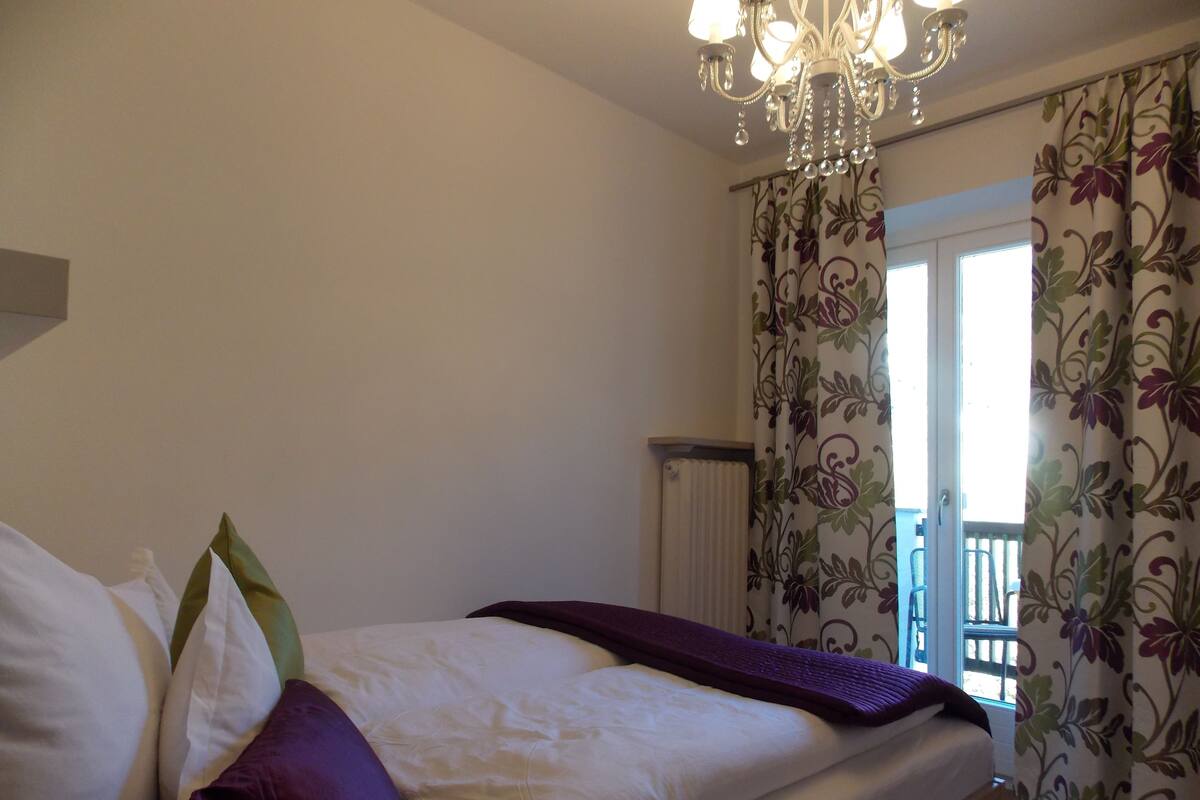A bedroom with a bed, a chandelier, and floral curtains.