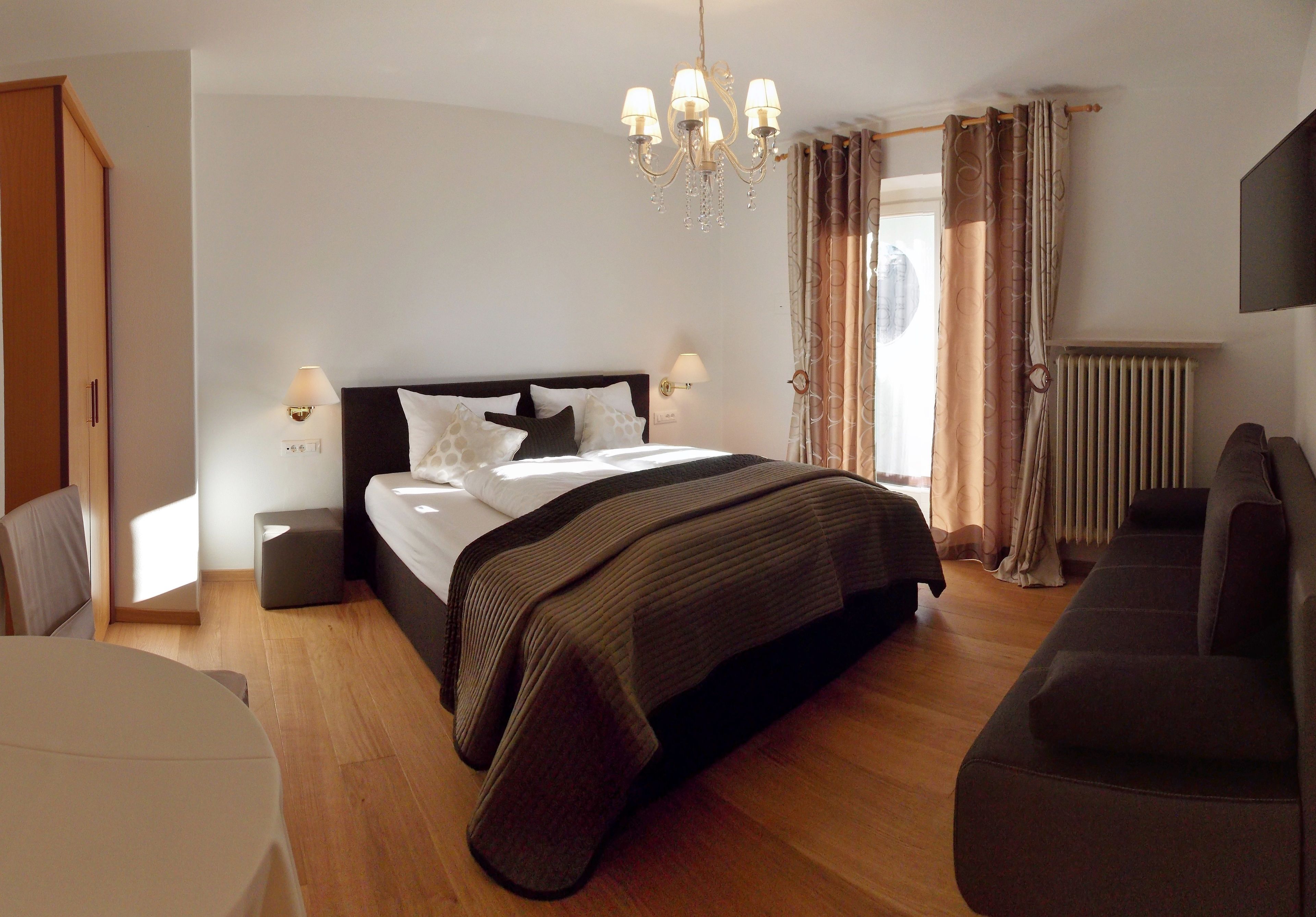 A bedroom with a large bed, bedside lamps, a chandelier, a radiator, and a sofa.