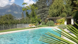 Piscina cristalina con sillas de descanso, rodeada de vegetación y vistas a la montaña.