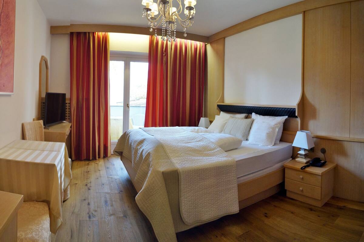 A hotel room with a bed, bedside table, lamp, and a desk with a chair.