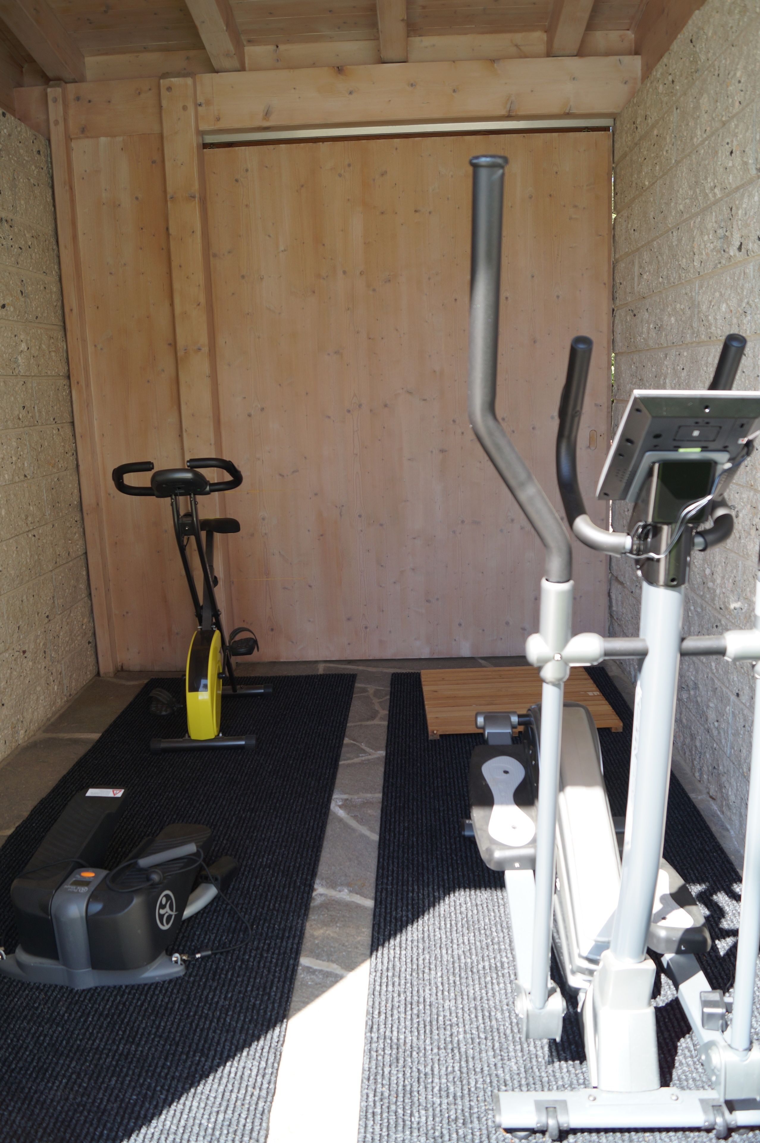 A small, enclosed gym area with a stationary bike, elliptical, and weight machine.