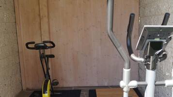 A small, enclosed gym area with a stationary bike, elliptical, and weight machine.