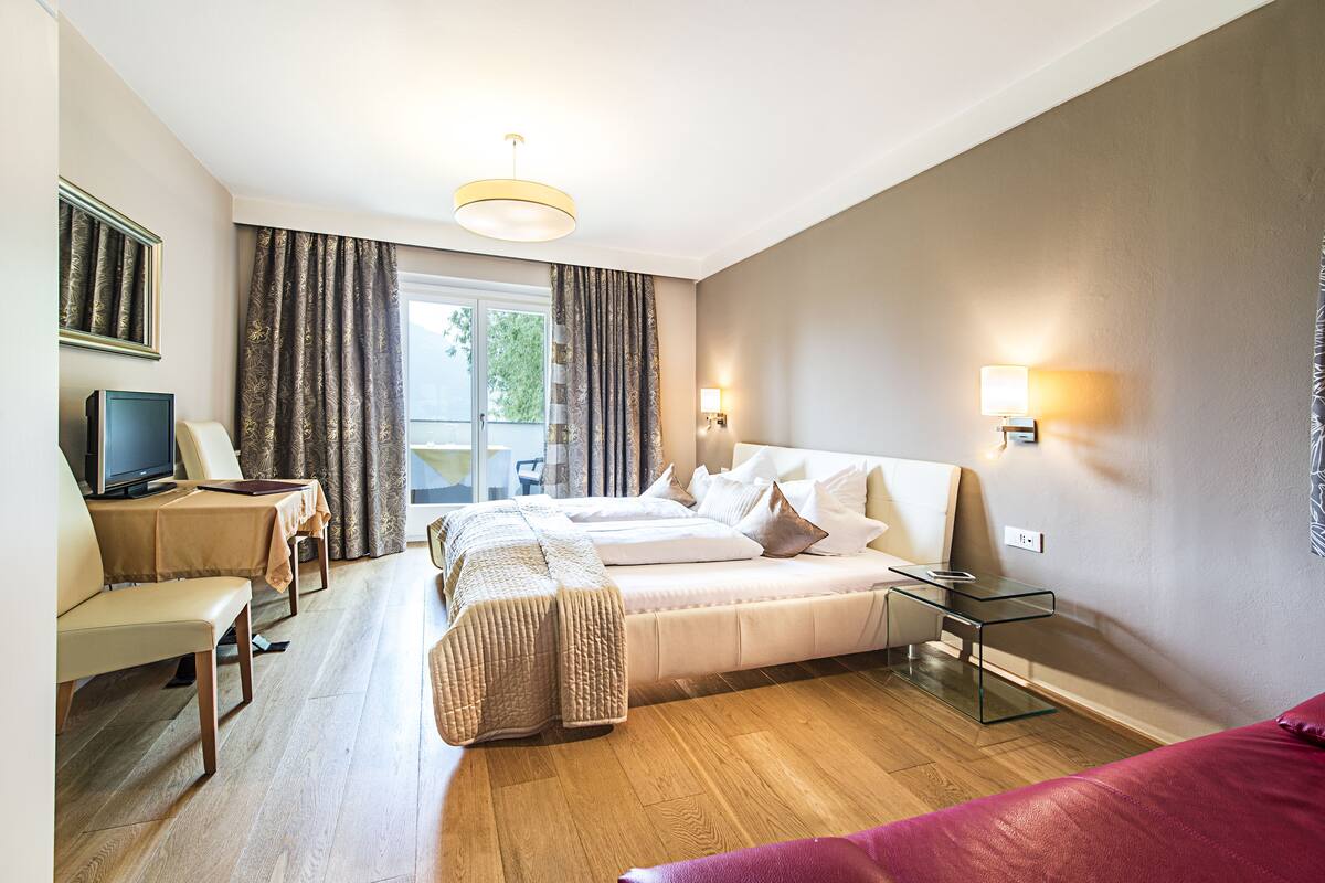 A hotel room with a bed, a desk, a chair, a TV, and a window with curtains.
