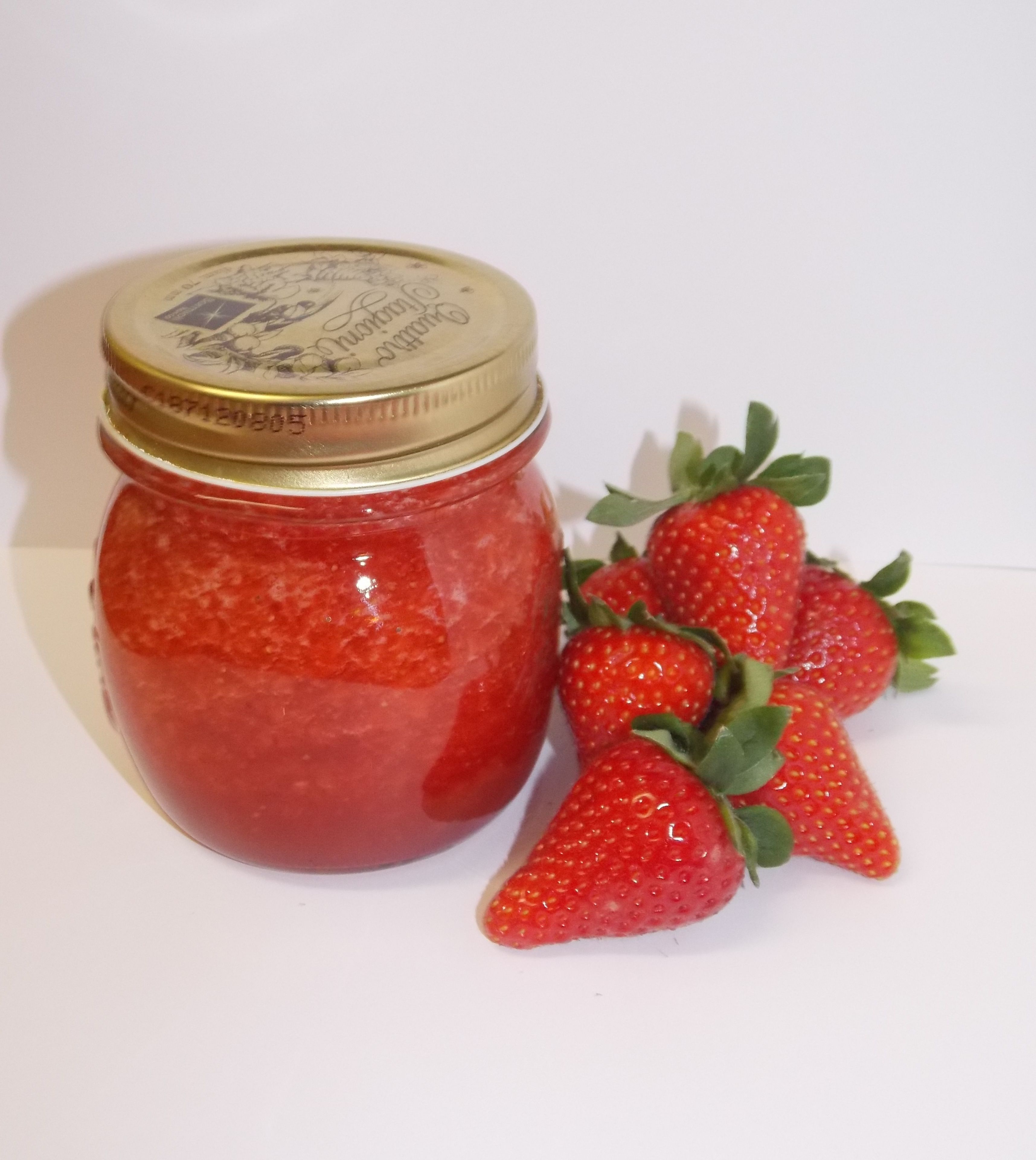 Ein Glas Erdbeermarmelade mit goldfarbenem Deckel und ein Strauß frischer Erdbeeren daneben.
