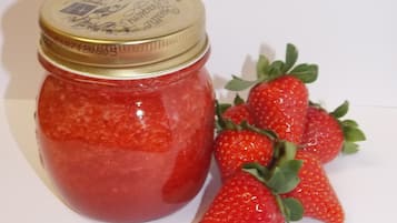 Ein Glas Erdbeermarmelade mit goldfarbenem Deckel und ein Strauß frischer Erdbeeren daneben.