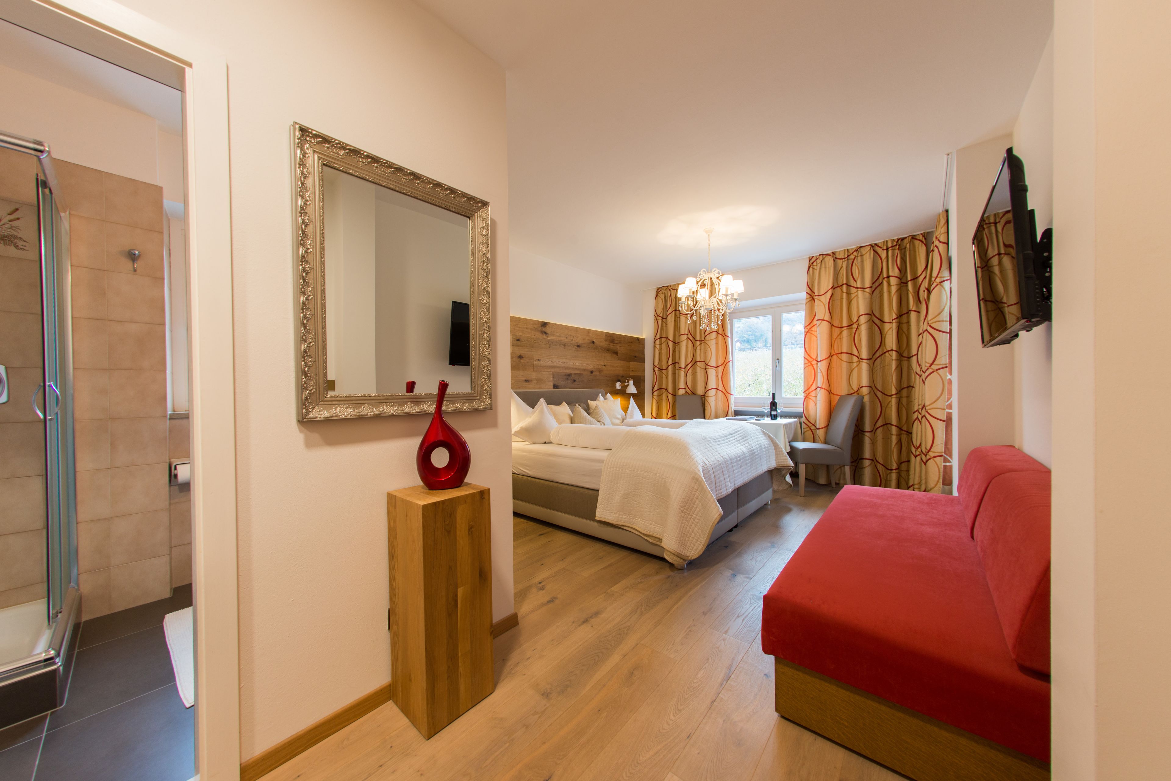 Quarto de hotel com cama, escrivaninha, cadeira, televisão, espelho e chuveiro.